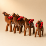 Four wooden camel figurines with red saddle packs on a beige background