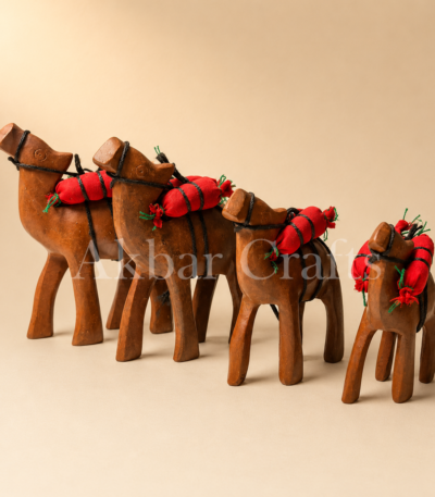 Four wooden camel figurines with red saddle packs on a beige background